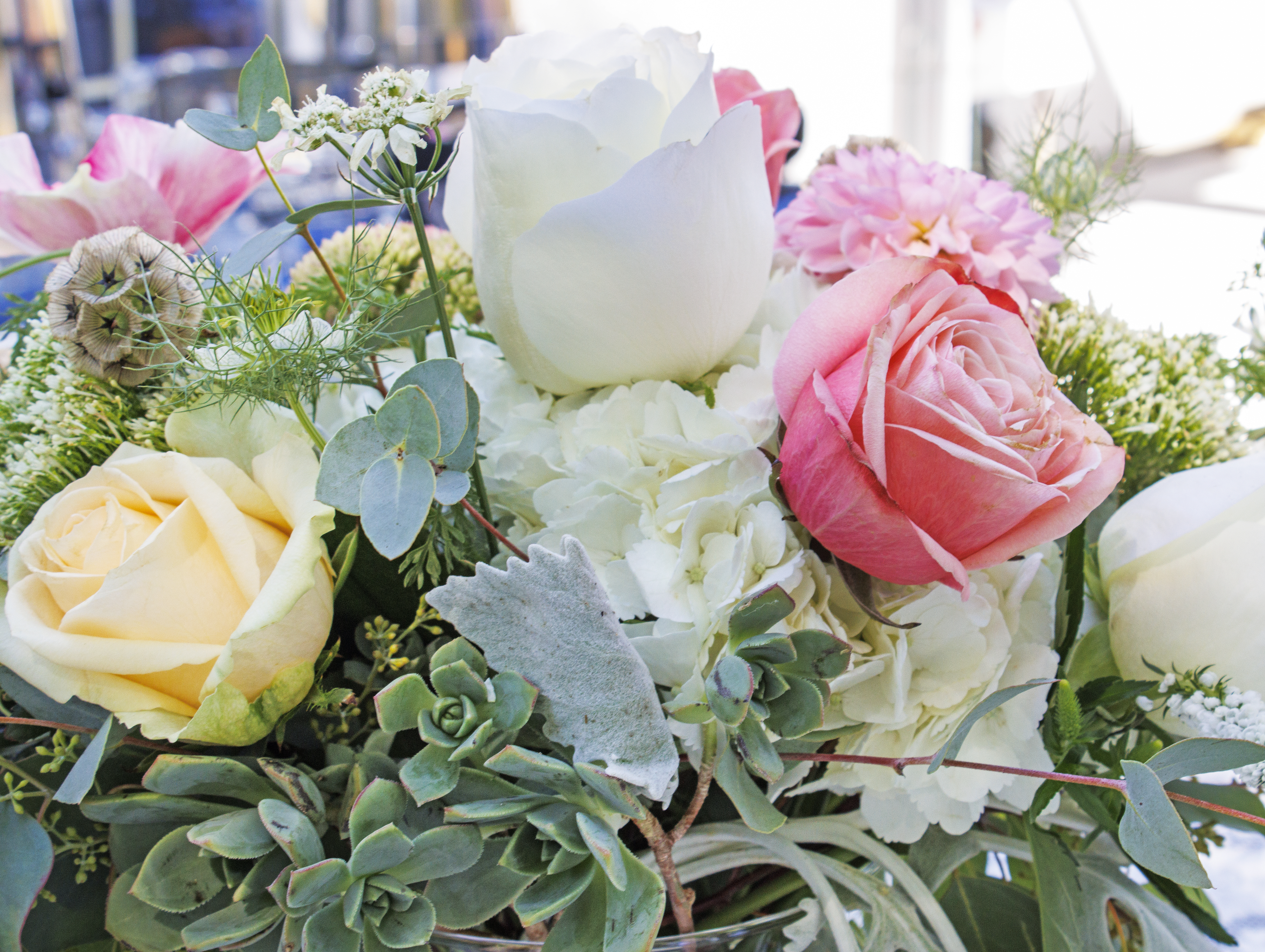 A bouquet of flowers, including light pink and white roses, green succulents, white hydrangeas, and pale yellow roses arra...
