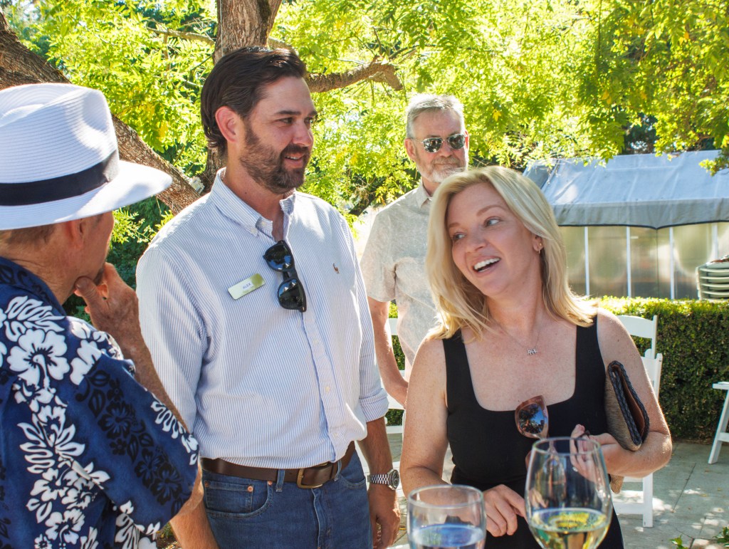 A group of friends gather in a park, laughing and socializing at a gathering: three men and a woman laugh, including one w...
