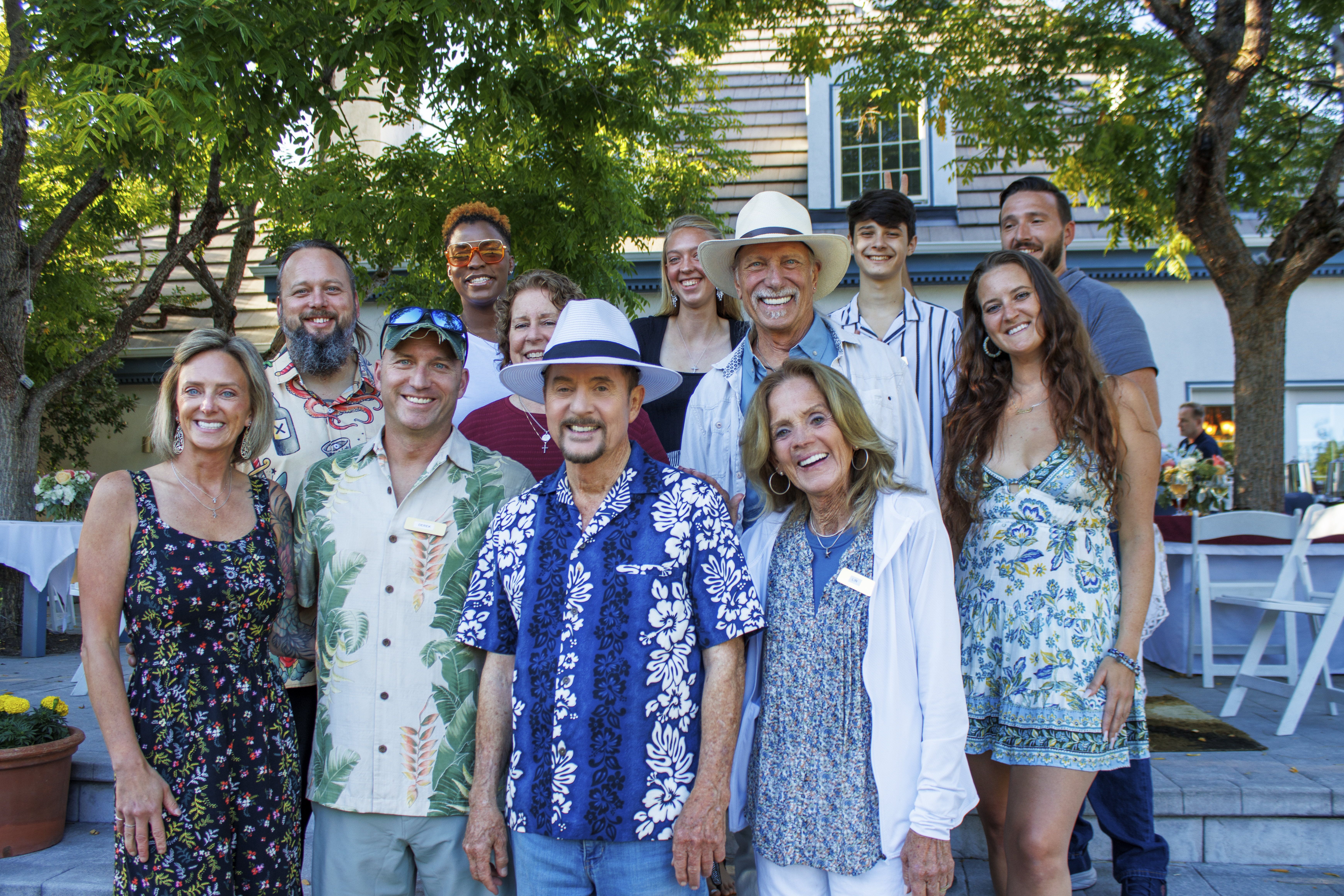 A group of people standing on a patio, a tree, and a house serving as the backdrop, not much distinction evident between t...